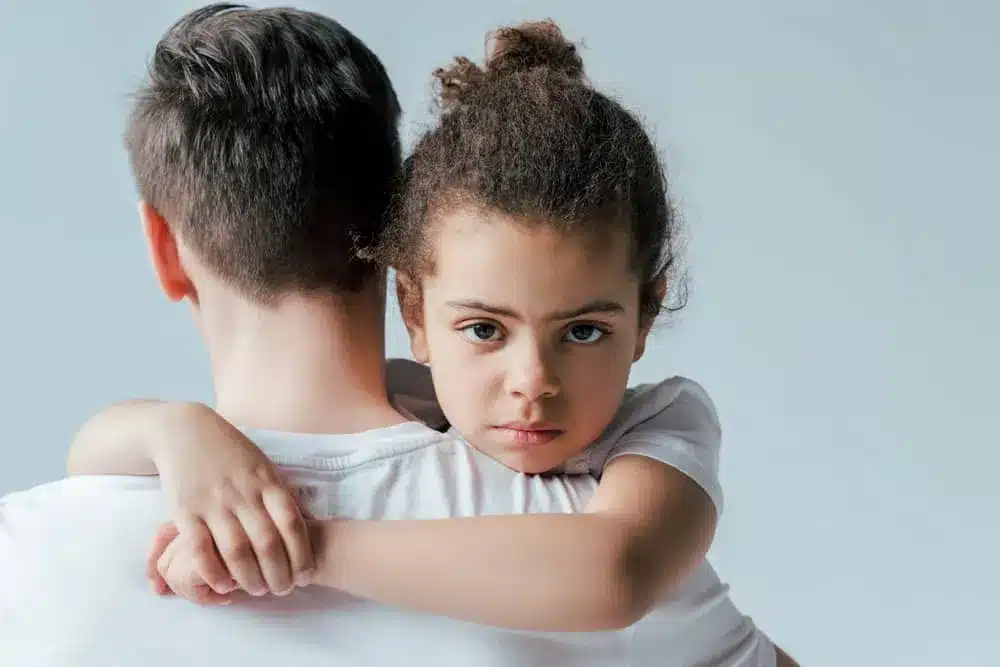 A sad child clings to father during custody process